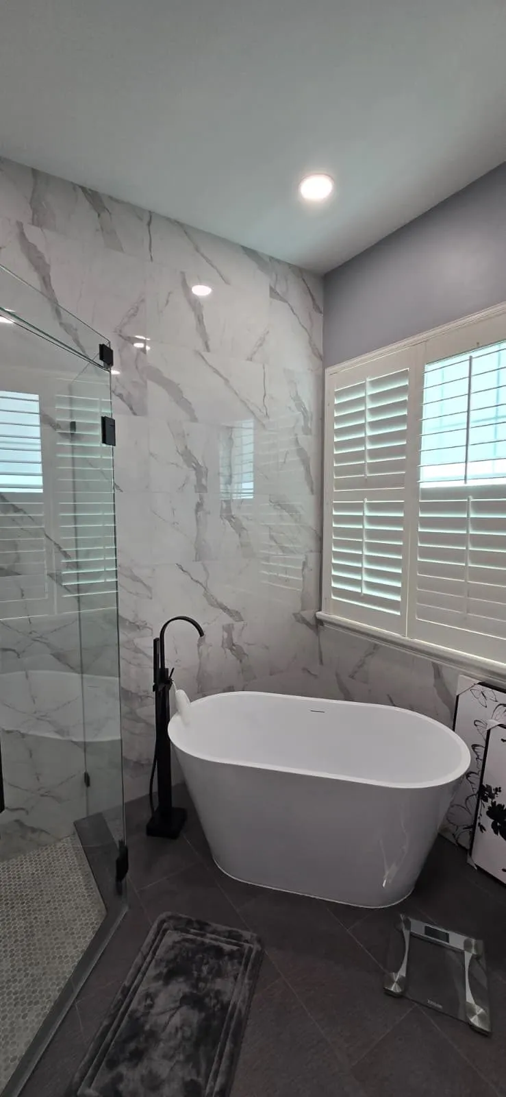 Freestanding tub against marble-look porcelain wall with black floor faucet
